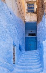 Light blue worn stone steps leading up to a blue door in Chefchaouen medina, Morocco.