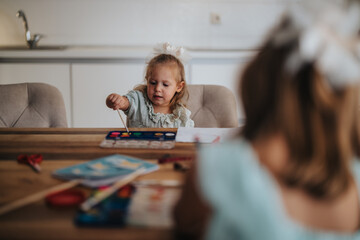 A mother and her young daughters engaging in a fun and creative painting activity, highlighting family bonding and creativity in a cozy home setting.