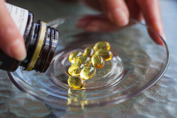 Close up Omega 3 supplements fell out of a bottle on a glass plate. Food additives. Selective focus.