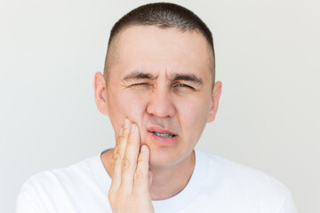 Naklejka premium Young man suffering from toothache, gum inflammation, holding his cheek with his hand. Dental care. Dentistry. Oral care