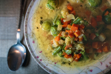 A close-up of vibrant mixed vegetables including carrots, green beans, and Brussels sprouts in a rich, creamy sauce, served artistically on a porcelain plate. Perfect healthy polish soup