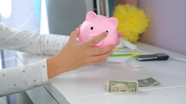 Close-up of young girl eagerly empties her pink piggy bank, excited to see how much she is saved as she learns the value of managing her own money, slow motion