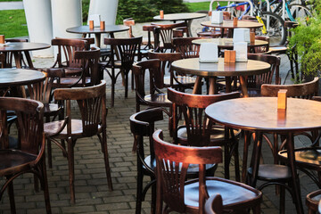 An empty outdoor cafe terrace with vintage wooden tables and chairs neatly arranged, waiting for customers on a sunny day, with a cozy and welcoming atmosphere.