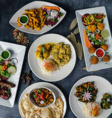 Dinner table decorated with mouthwatering Indian cuisine colorful plates with rice, spicy curries, crispy naan bread, and fresh salads adorned with herbs—garnishes of bright vegetables and chutneys.