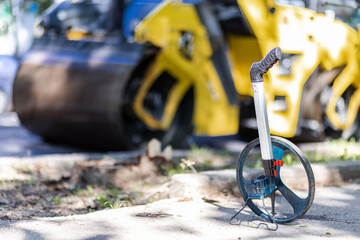 Measuring wheel resting on a concrete surface near a road construction site during daytime with a...