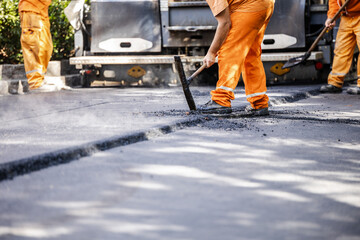 Workers in bright orange uniforms engage in asphalt paving on a city street during daytime in a...