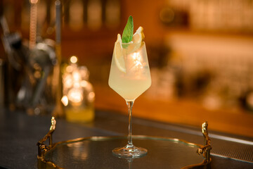 Tall stemmed glass filled with a white cocktail with ice, lemon slices and a green leaf