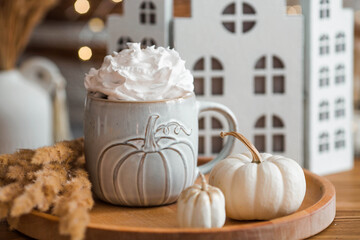 Delicious pumpkin latte with whipped cream and cinnamon in a mug on the table in the living room interior. Autumn decor in the house. Scandinavian style.