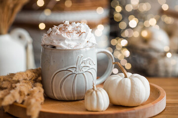 Delicious pumpkin latte with whipped cream and cinnamon in a mug on the table in the living room interior. Autumn decor in the house. Scandinavian style.