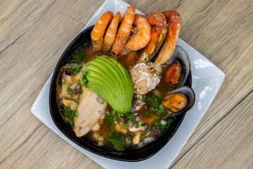 Overhead view of seafood shellfish soup with shrimp, crab, avocado, white fish, and mussels served hot in a bowl