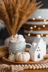 Delicious pumpkin latte with whipped cream and cinnamon in a mug on the table in the living room interior. Autumn decor in the house. Scandinavian style.