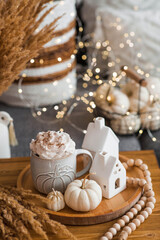 Delicious pumpkin latte with whipped cream and cinnamon in a mug on the table in the living room interior. Autumn decor in the house. Scandinavian style.