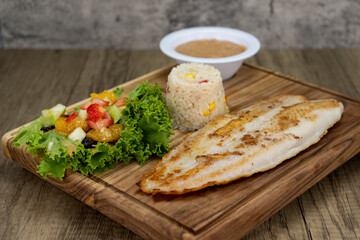 Grilled Basa fish fillet dinner served with rice and beans on a wooden platter