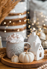 Delicious pumpkin latte with whipped cream and cinnamon in a mug on the table in the living room interior. Autumn decor in the house. Scandinavian style.