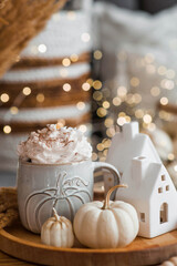 Delicious pumpkin latte with whipped cream and cinnamon in a mug on the table in the living room interior. Autumn decor in the house. Scandinavian style.