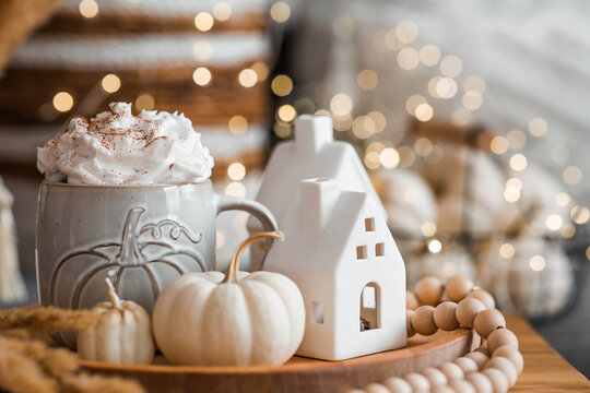 Delicious pumpkin latte with whipped cream and cinnamon in a mug on the table in the living room interior. Autumn decor in the house. Scandinavian style.