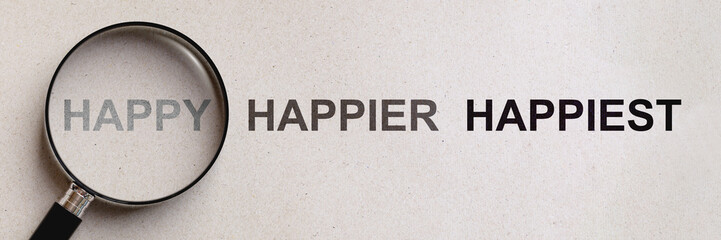 Happy inside magnifying glass among wording happier and happiest on paper. Concept of comparison of...