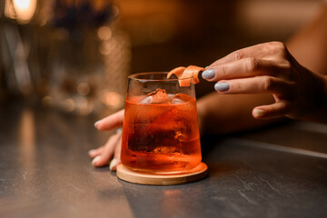 Female hands decorate a glass with a drink and ice with a piece of peel