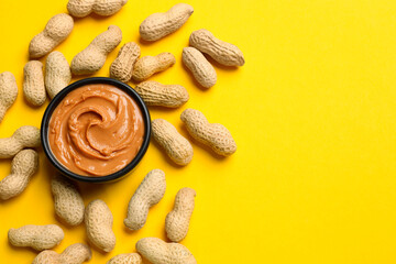 Tasty peanut butter in bowl and groundnuts on yellow table, flat lay. Space for text