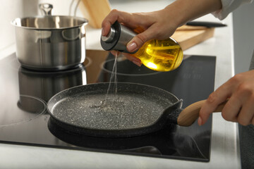 Woman pouring oil into frying pan on cooktop in kitchen, closeup