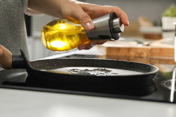 Woman with bottle of oil and frying pan in kitchen, closeup