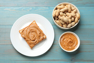 Tasty sandwich with peanut butter and nuts on light blue wooden table, flat lay