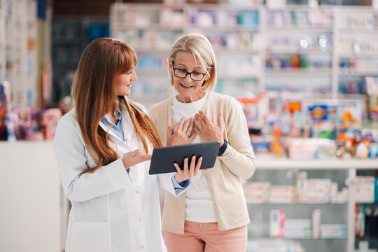 Pharmacist showing information on digital tablet to customer in pharmacy