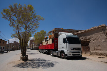 Large white lorry truck with loaded goods on red trailer over blue sky in small town of South America. Transportation vehicle, transportation concept.