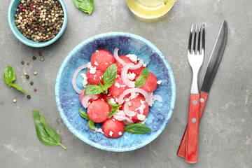 Delicious watermelon salad with feta cheese, mint and onion in bowl served on grey textured table, flat lay