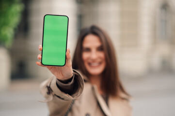 Smiling woman showing green screen smartphone on the street