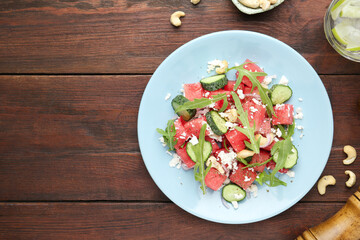 Tasty salad with watermelon, feta cheese, cashews and arugula on wooden table, flat lay