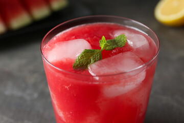 Tasty watermelon drink in glass and mint on blurred background, closeup