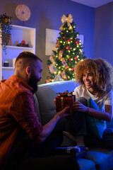 Man giving christmas gift to woman on sofa
