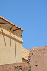 Adobe walls and traditional Moroccan rooftops with wooden beams casting shadows against a vibrant blue sky in Marrakech
