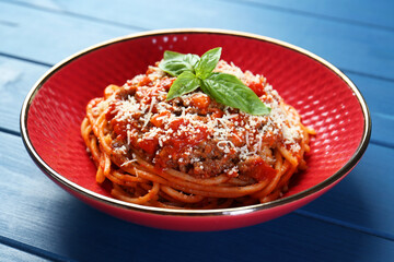 Delicious pasta bolognese with basil on blue wooden table, closeup