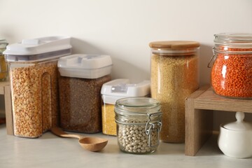 Different types of cereals and legumes in containers on light marble table in kitchen