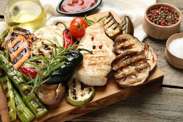 Delicious grilled vegetables and chicken breast on wooden table, closeup