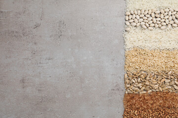 Different types of cereals, legumes and seeds on grey textured table, flat lay. Space for text