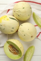 Fresh whole and cut honeydew melons on white wooden table, flat lay