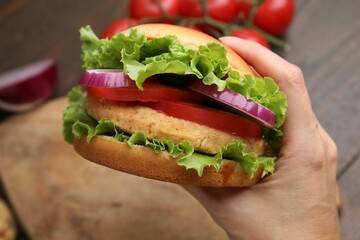 Woman holding vegetarian burger with chickpea cutlet at table, closeup