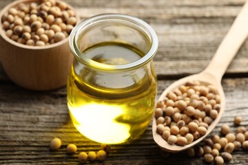 Cooking oil in jar and soybeans on wooden table, closeup