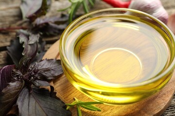 Cooking oil in bowl, red basil and rosemary on wooden table, closeup