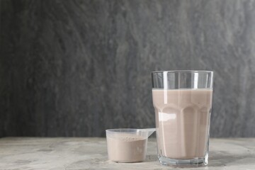Delicious protein shake in glass and scoop with powder on grey table, space for text