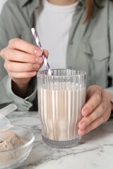 Woman with glass of protein cocktail at white marble table, closeup