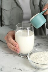Making protein cocktail. Woman adding powder into glass with milk at white marble table, closeup