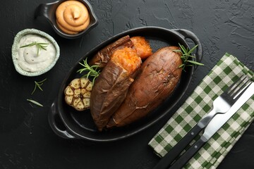 Tasty cooked sweet potatoes served with rosemary and sauces on black table, top view