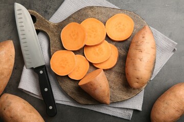 Fresh raw sweet potatoes and knife on gray table, top view