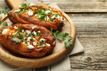Tasty cooked sweet potatoes with feta cheese, green onion and parsley on wooden table, closeup