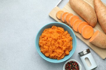 Tasty mashed sweet potato in bowl, fresh vegetables and spices on gray table, flat lay. Space for text