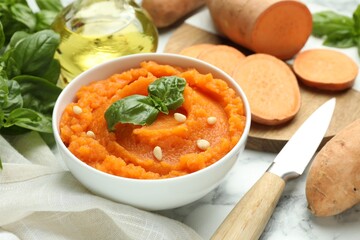 Tasty mashed sweet potato with basil, seeds in bowl and ingredients on table, closeup